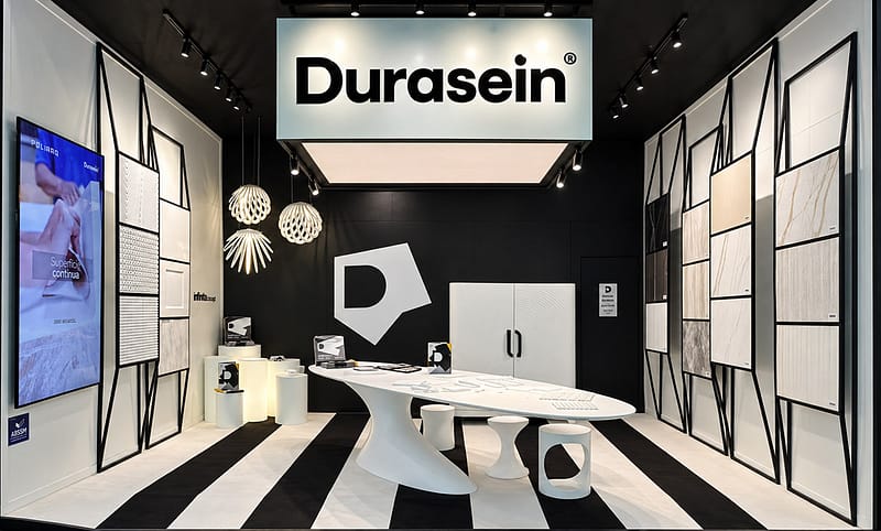 Vista geral do estande da Durasein na ForMóbile 2026, com mesa central, painéis expositivos e luminárias.